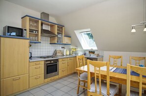 A kitchen with wooden cabinets, a stove, and a dining table with chairs. - Die Ferienwohnung Nr. 03 im Haus Inselblick - Haus Inselblick (Göhren)