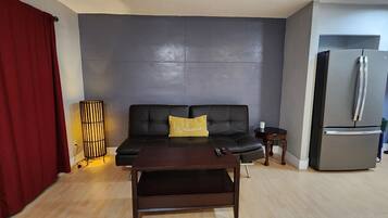A living room with a sofa, a coffee table, a red curtain, a lamp, and a refrigerator.