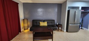 Sala de estar con sofá, mesa de centro, cortina roja, lámpara y refrigerador.