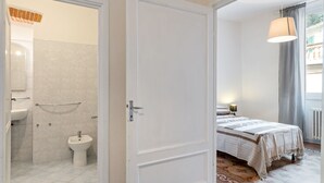 A hotel room with a bathroom, a bed with a patterned bedspread, and a hanging lamp. - Appartamento Galgani -Affitti Brevi Italia (Lucca)