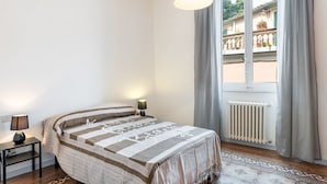 A bedroom with a bed, a nightstand, a lamp, a window with curtains, and a radiator. - Appartamento Galgani -Affitti Brevi Italia (Lucca)