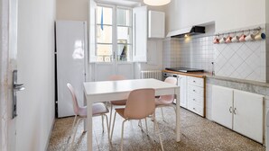 A compact kitchen with white cabinets, a dining table with chairs, a hanging light fixture, and a tiled backsplash. - Appartamento Galgani -Affitti Brevi Italia (Lucca)
