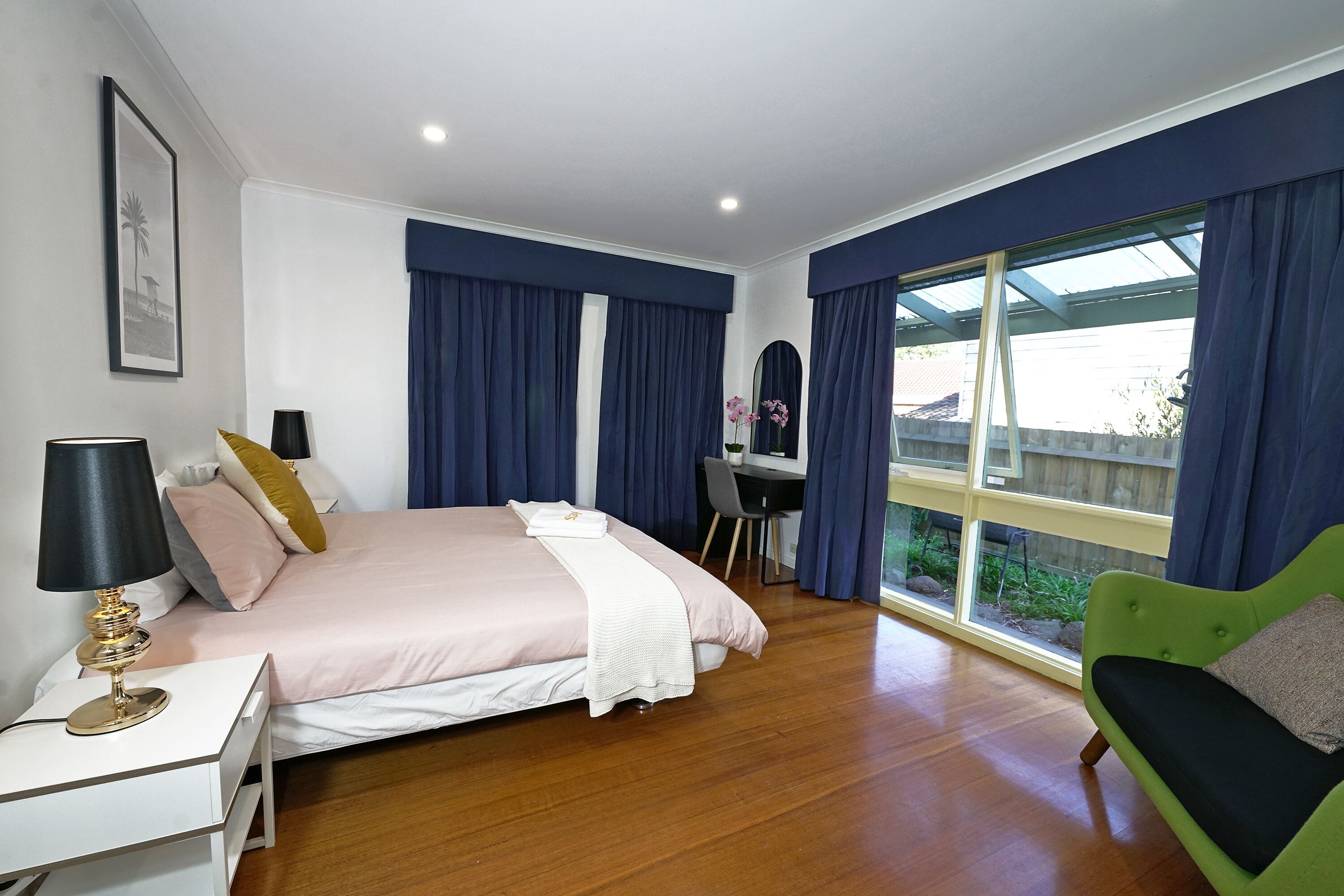 Un dormitorio con cama, mesita de noche, lámpara y sofá verde.
