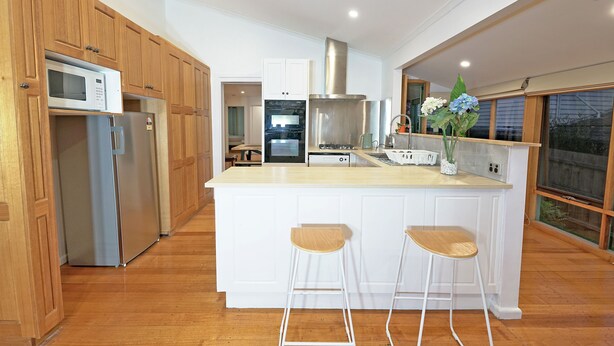 A modern kitchen with wooden cabinets, a stainless steel refrigerator, a microwave, and a large island with bar stools. - Family Holiday Entire House 8BRM Vermont (Vermont)