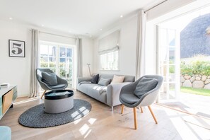 A modern living room with a grey sofa, two armchairs, a coffee table, and a large window providing natural light.