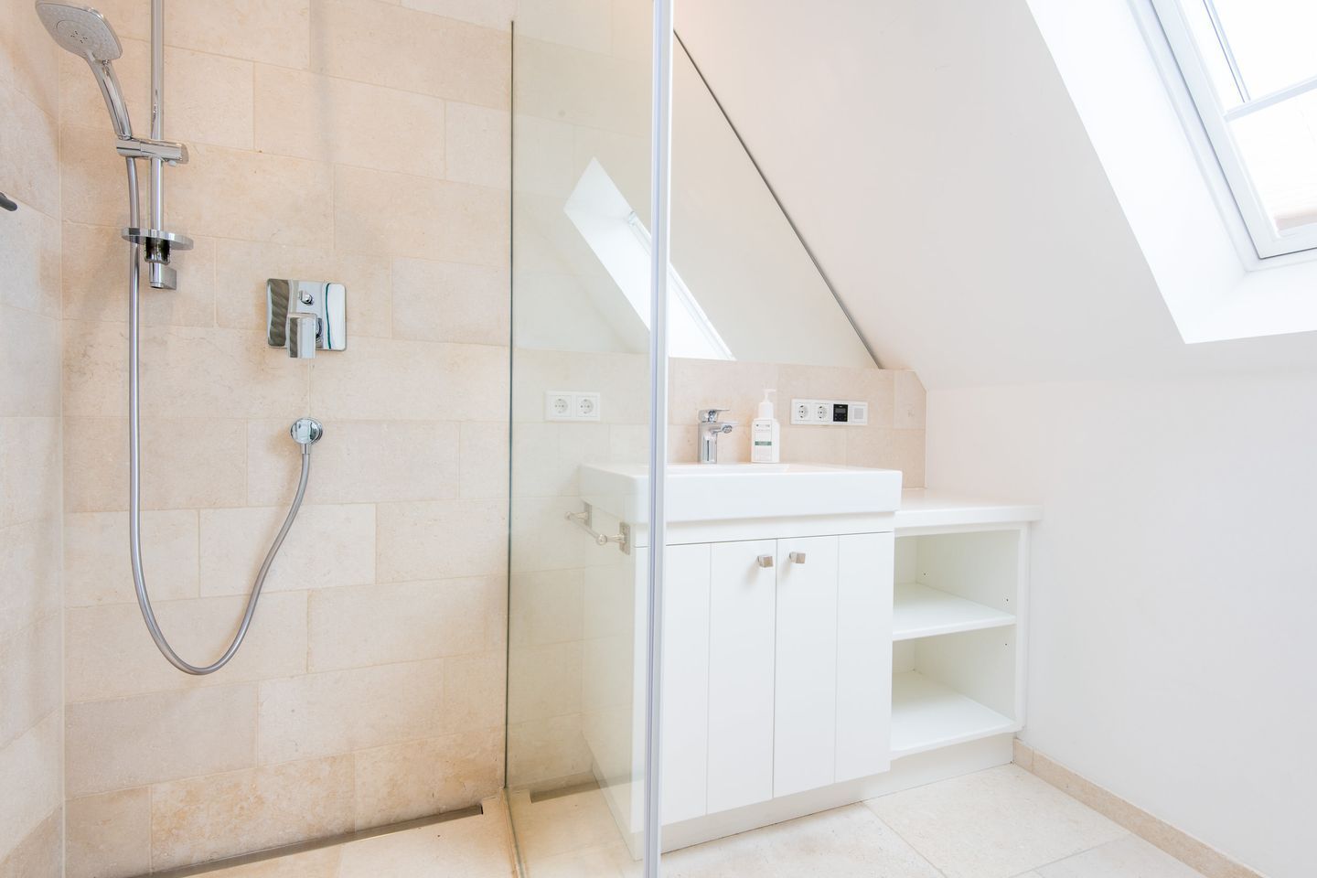 A modern bathroom with a glass-enclosed shower, white cabinetry, and a skylight.