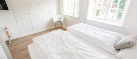 A bedroom with two beds, a wardrobe, a chair, and a window with curtains.
