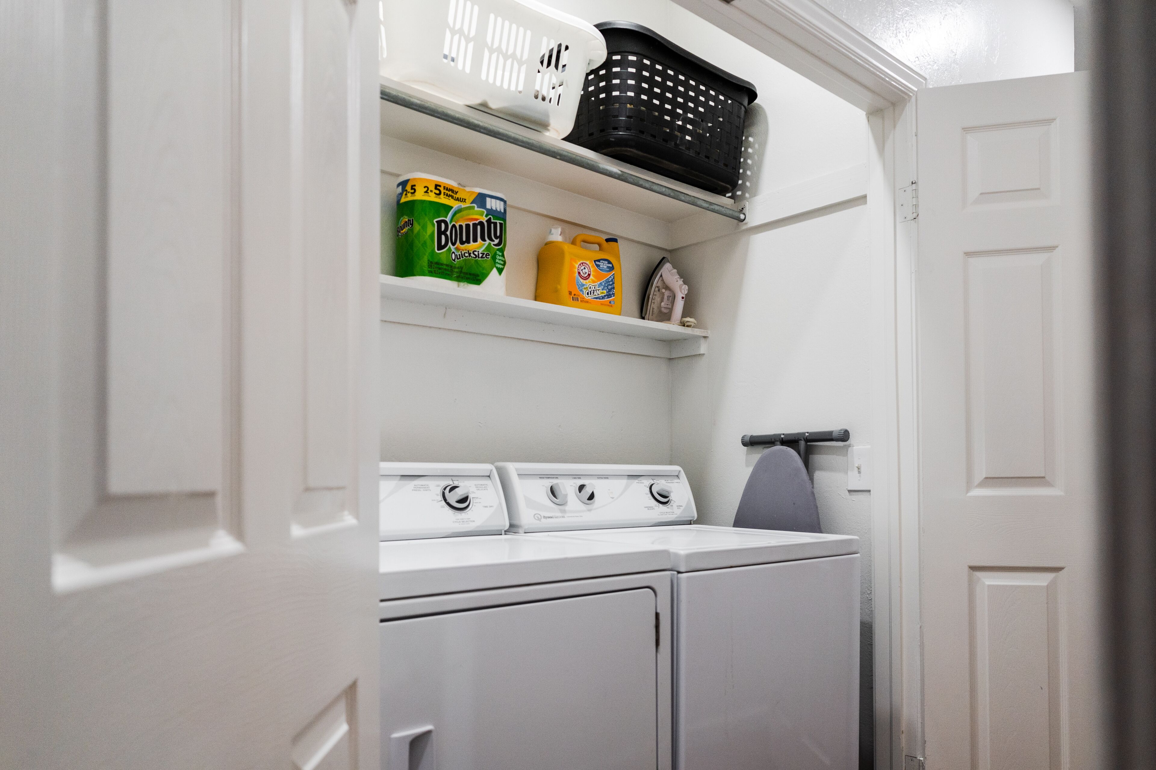Un espace buanderie comprenant un lave-linge, un sèche-linge et des étagères pour ranger les produits de nettoyage.