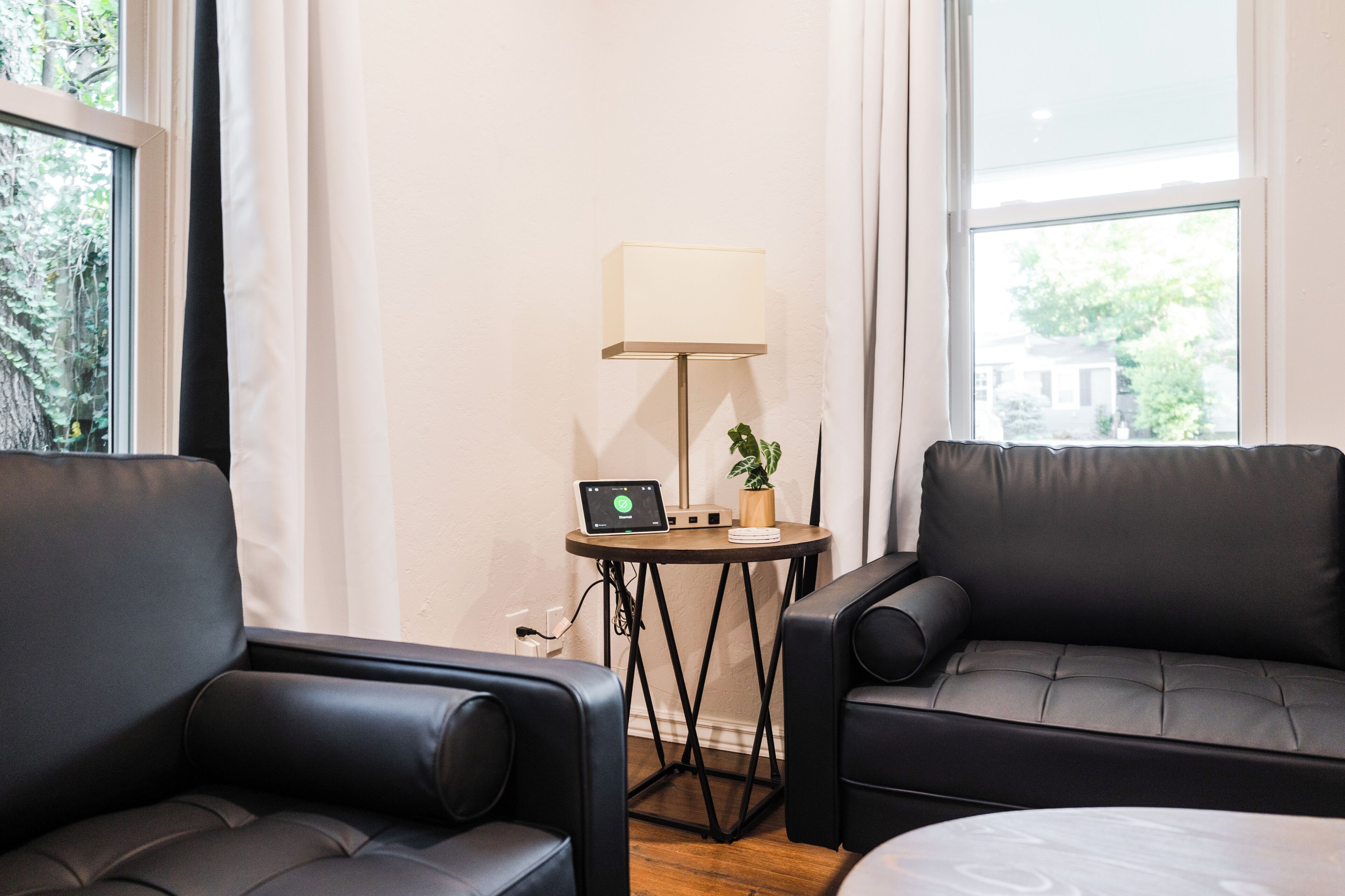 Una habitación con dos sofás de cuero negro, una mesita redonda con lámpara y un ordenador portátil.