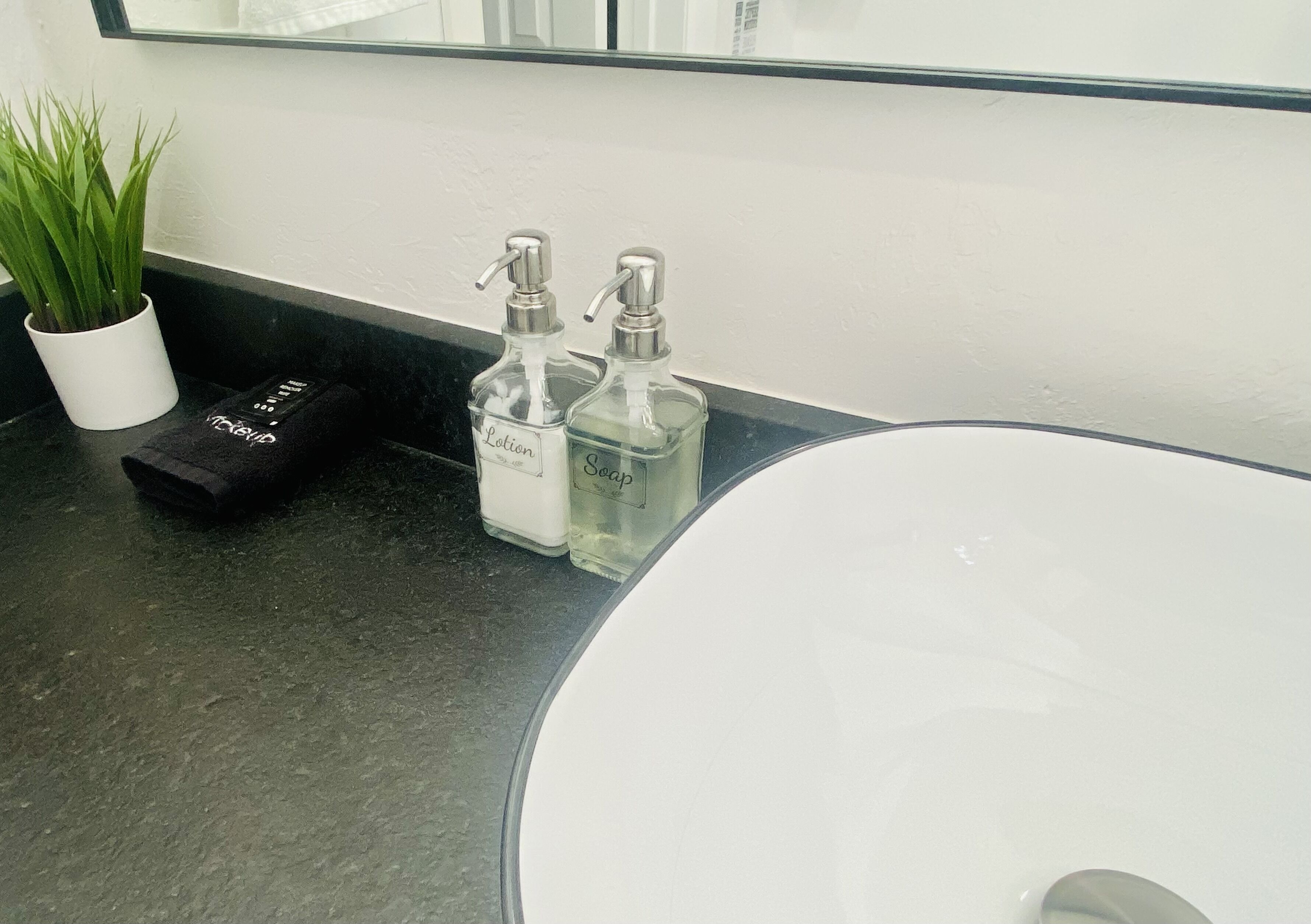A bathroom sink with two clear glass soap dispensers labeled "Lotion" and "Soap" on a black countertop.