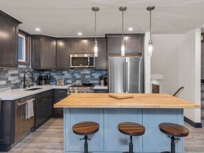 Cozinha moderna com armários de madeira escura, geladeira de aço inoxidável, uma ilha grande com banquetas e iluminação pendente.