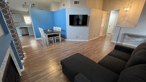 Una sala de estar moderna con un sofá de color oscuro, un comedor con mesa y sillas, y una cocina al fondo.
