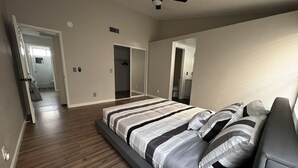 Un dormitorio con cama, ventilador de techo y pasillo que lleva a un baño.