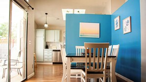 Un comedor con mesa y sillas, una cocina al fondo y una pared azul decorada con obras de arte.