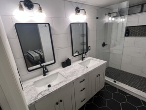 A modern bathroom with two sinks, a large mirror, and a shower area.