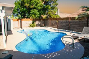 A swimming pool with a curved edge, surrounded by a concrete deck and a wooden fence.