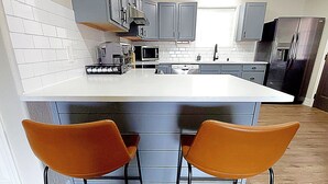 A modern kitchen with a central island, grey cabinets, and a white countertop. There are two orange chairs at the island. - Beautiful Casita, Pet Friendly, Full RV Hookups & Boat Parking (Page)