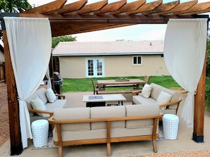 Un espace extérieur abrité, avec des places assises, comprenant un banc en bois et une table, le tout entouré de rideaux blancs.