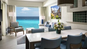 A hotel room with a large window offering a view of the ocean, a dining area with a table and chairs, a sofa with patterned cushions, and a decorative vase with flowers. - 2 Bedroom - Westin Lagunamar Ocean Resort - Full Resort Access (Cancún)