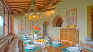 Un espace repas avec une longue table en bois dressée pour le repas, des bancs le long du mur et une cheminée en briques.