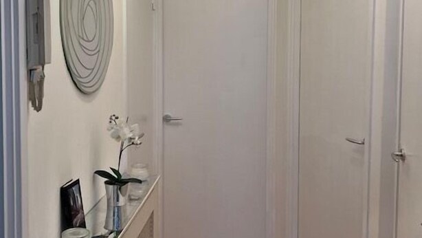 A hallway with a white door, a ceiling light fixture, a wall-mounted light, and a radiator. - West End 1-Bed Apt, Sleeps 2 with Wi-Fi (London)