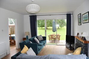 Ein Wohnzimmer mit Sofa, Fernseher und Kamin, ein Essbereich mit Tisch und Stühlen sowie eine große Glasschiebetür, die zu einem Garten führt.