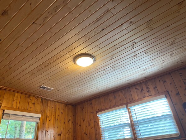 A room with wooden panel walls, a ceiling with horizontal wooden planks, and a window with blinds.