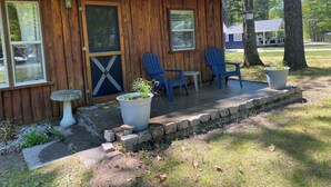 Une cabane en bois avec deux chaises Adirondack bleues, une petite table et une plante en pot sur le porche.