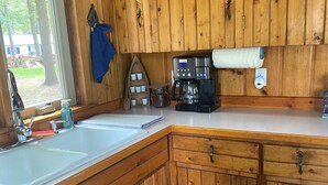 Une cuisine rustique, située dans une cabane en bois, avec un grand évier, une machine à café et des placards en bois.
