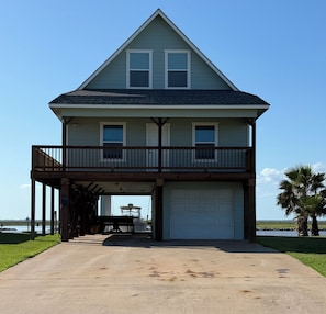 A two-story house with a balcony, a garage, and a view of the water. - Sargent Beach House Getaway - fish from the dock and walk to the beach! (Sargent)