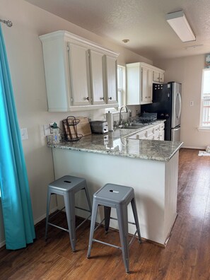 A kitchen with white cabinets, a black refrigerator, a granite countertop, and two grey stools.