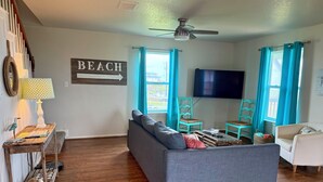 A living room with a sofa, a television, and a sign that reads 'BEACH'. - Sargent Beach House Getaway - fish from the dock and walk to the beach! (Sargent)