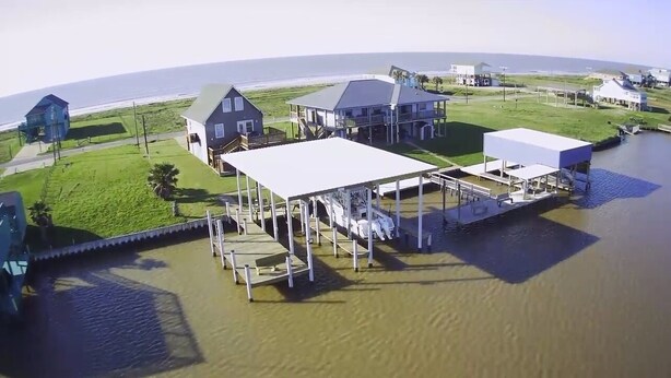 A waterfront property with multiple buildings, including a large house with a covered deck and a smaller structure. - Sargent Beach House Getaway - fish from the dock and walk to the beach! (Sargent)