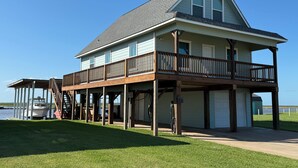 A two-story house with a covered porch, a garage, and a view of the water. - Sargent Beach House Getaway - fish from the dock and walk to the beach! (Sargent)