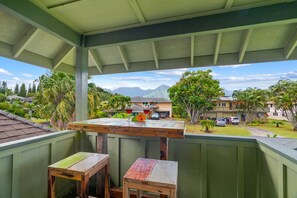 Ein überdachter Balkon mit Holztisch und -stühlen, der auf ein Wohngebiet mit Häusern und Bergen blickt.