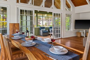 Un comedor con una larga mesa de madera dispuesta para cuatro personas, rodeado de grandes ventanales y vistas al exterior.