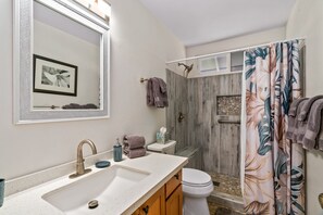 Ein Badezimmer mit einem Doppelwaschbecken, einer Toilette, einer Dusche mit Holztür und einem großen Spiegel.