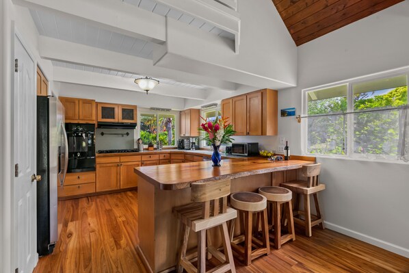 Una cocina con armarios de madera, una isla central con taburetes y vistas a zonas verdes por la ventana.