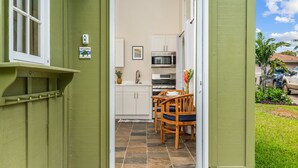 Ein schmaler Flur führt zu einer Küche mit weißen Schränken, einer Mikrowelle und einem Essbereich mit Holztischen und einer Tischplatte.
