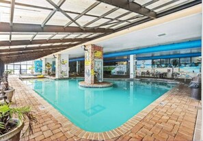 An indoor swimming pool with a brick floor, columns with graffiti, and a covered ceiling. - Impressive Oceanfront Suite on the 11th Floor (Myrtle Beach)