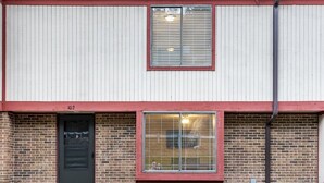 Ein zweistöckiges Gebäude mit einem roten Fensterrahmen, einer schwarzen Tür und einer Ziegel-Fassade.