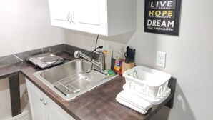 Una cocina con un lavamanos de acero inoxidable, un armario blanco y una frase motivacional en la pared.
