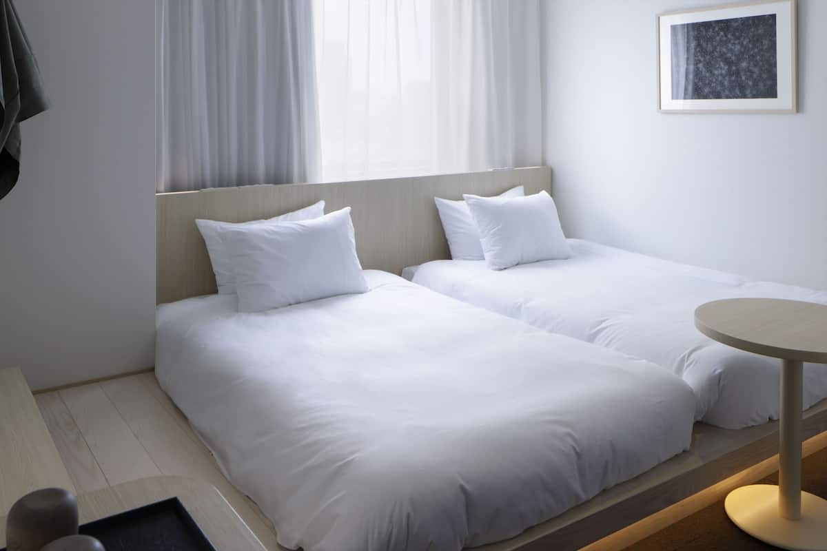 Habitación de hotel con dos camas individuales, una mesita y una silla.