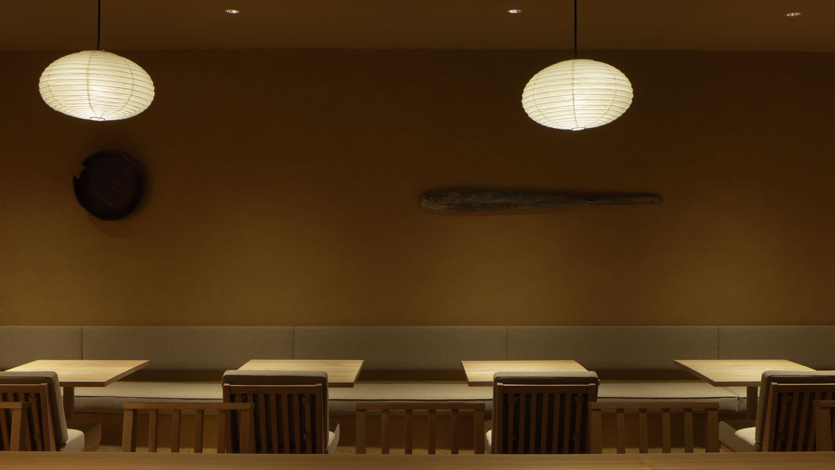 A restaurant with a long counter and multiple tables, two hanging paper lanterns, and a dark circular object on the wall.