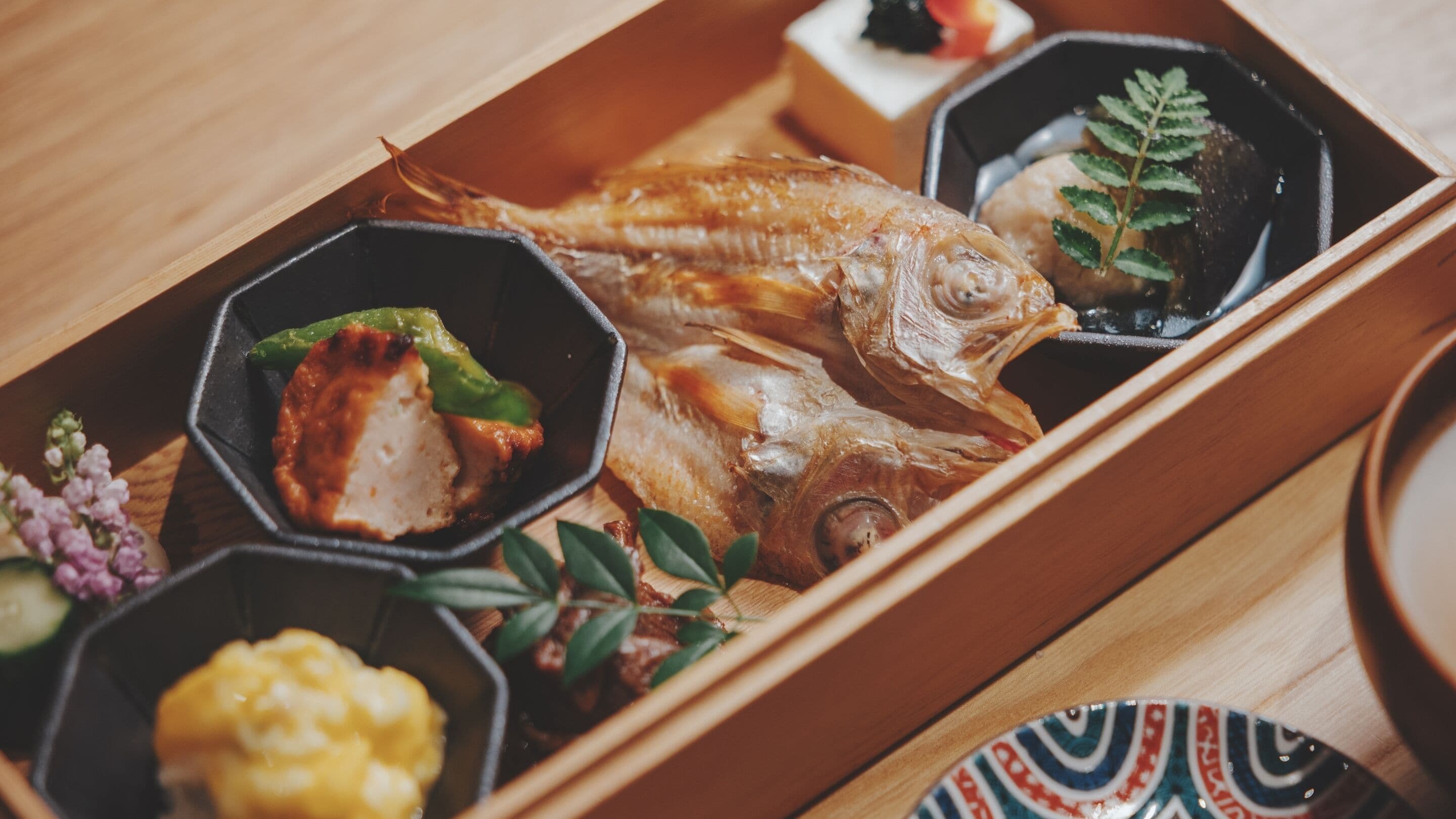 A wooden tray with a whole fish, a piece of meat, and several small bowls containing different food items.
