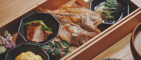 A wooden tray with a whole fish, a piece of meat, and several small bowls containing different food items.