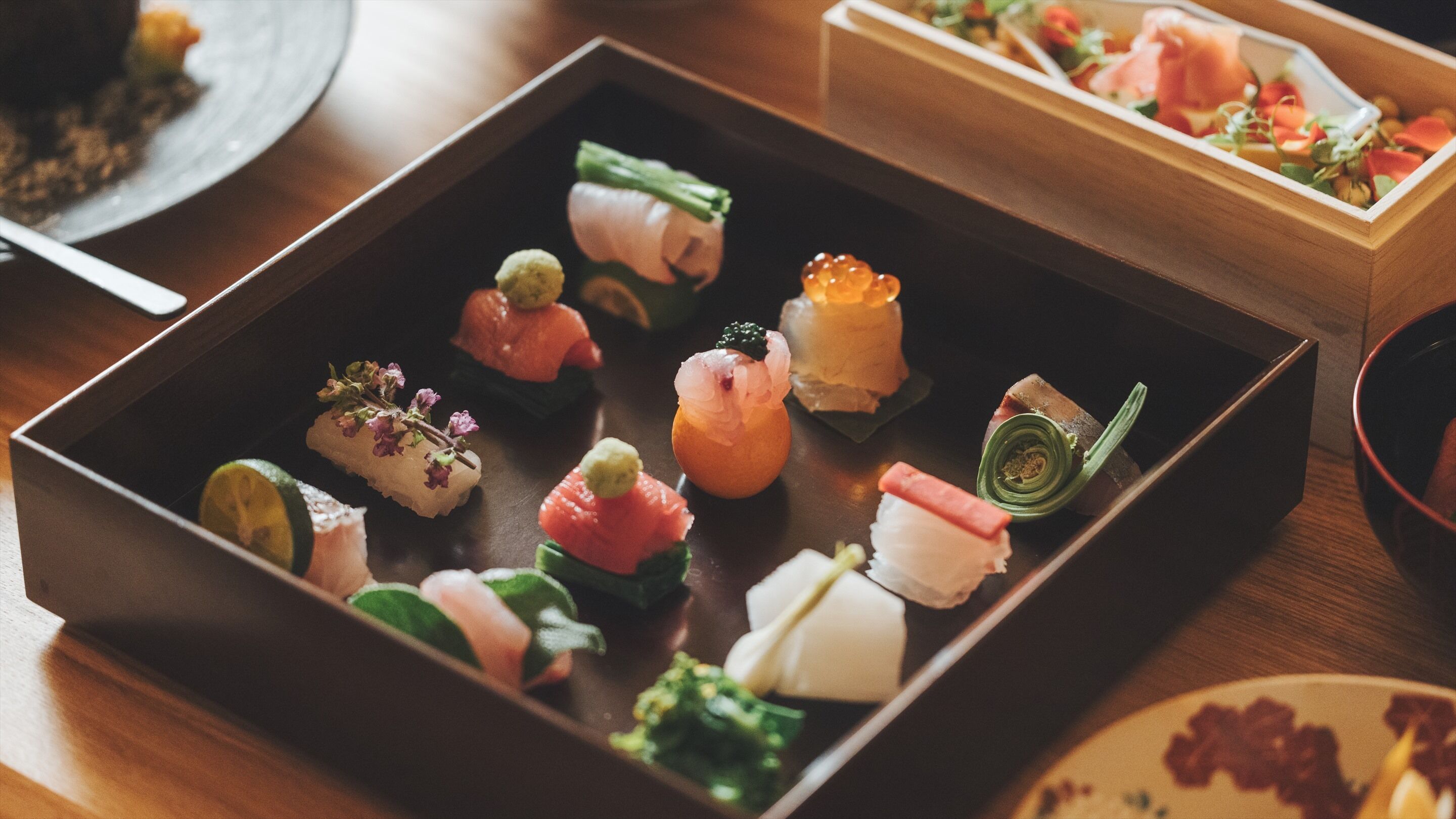 Une table en bois sur laquelle sont disposés divers aliments, notamment des sushis et d’autres amuse-gueules.