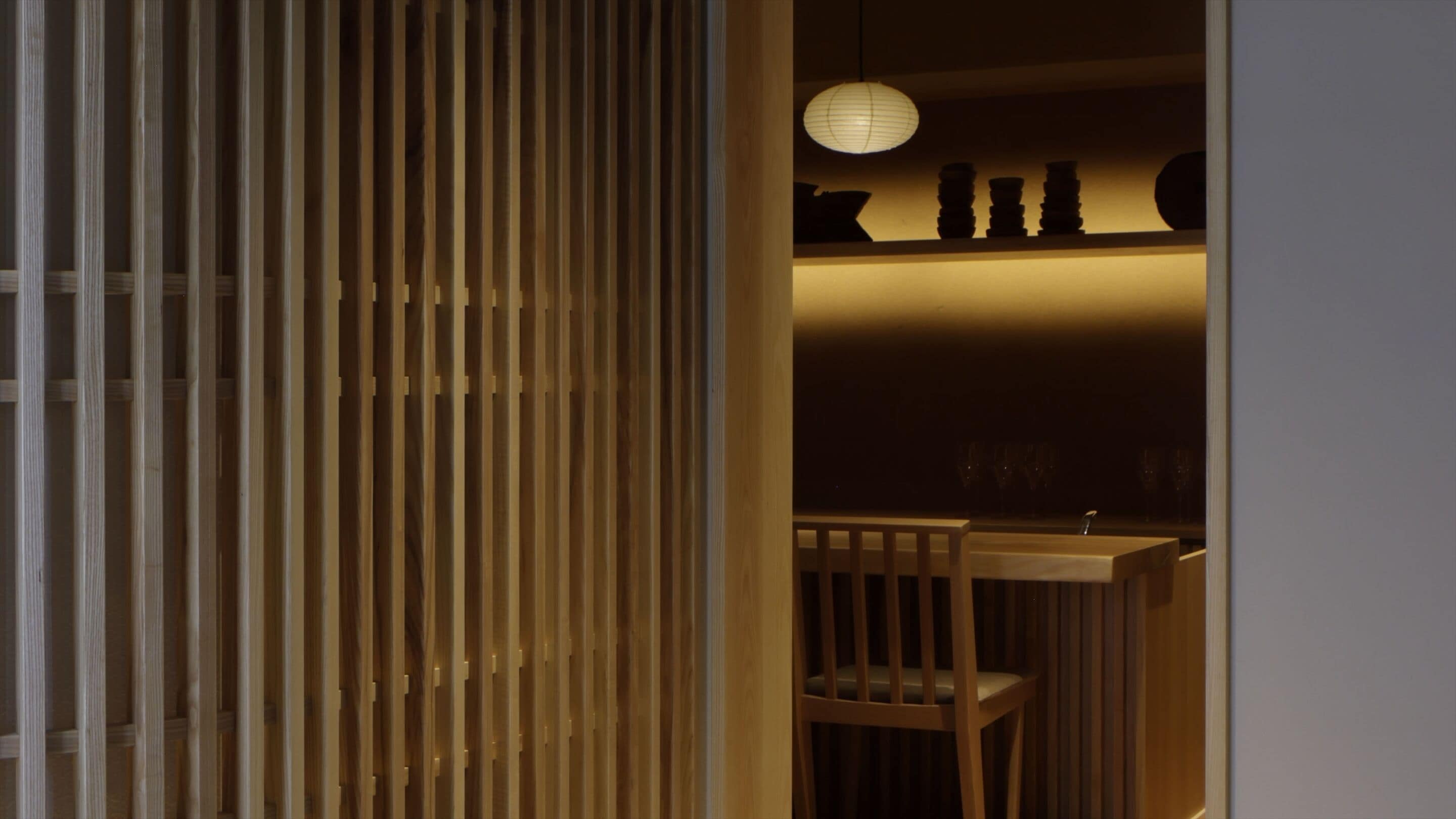 Una habitación con un separador de madera, un farol de papel colgante y una silla de madera.