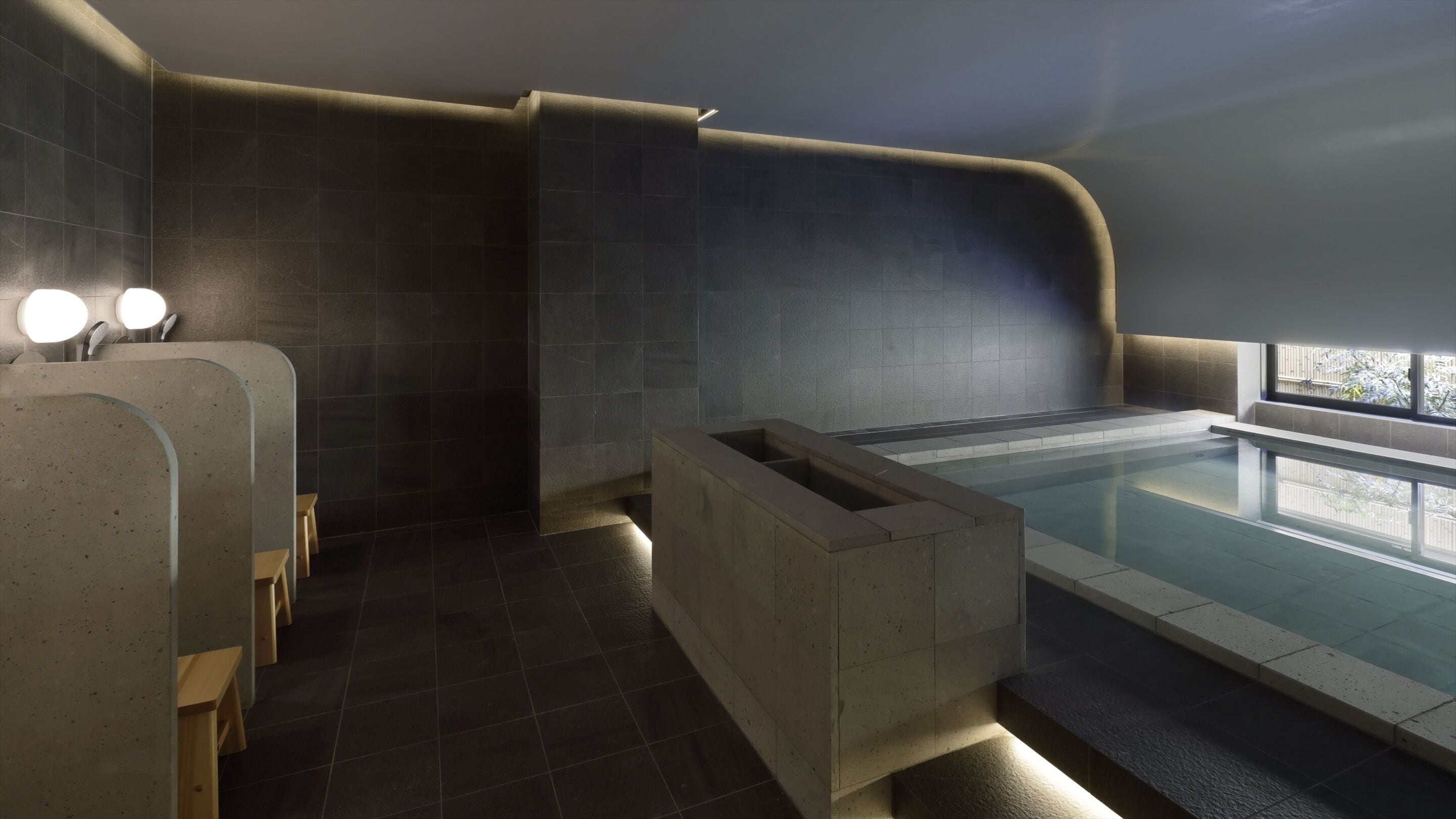 A modern spa area with a large bathtub, a small seating area, and a window providing natural light.
