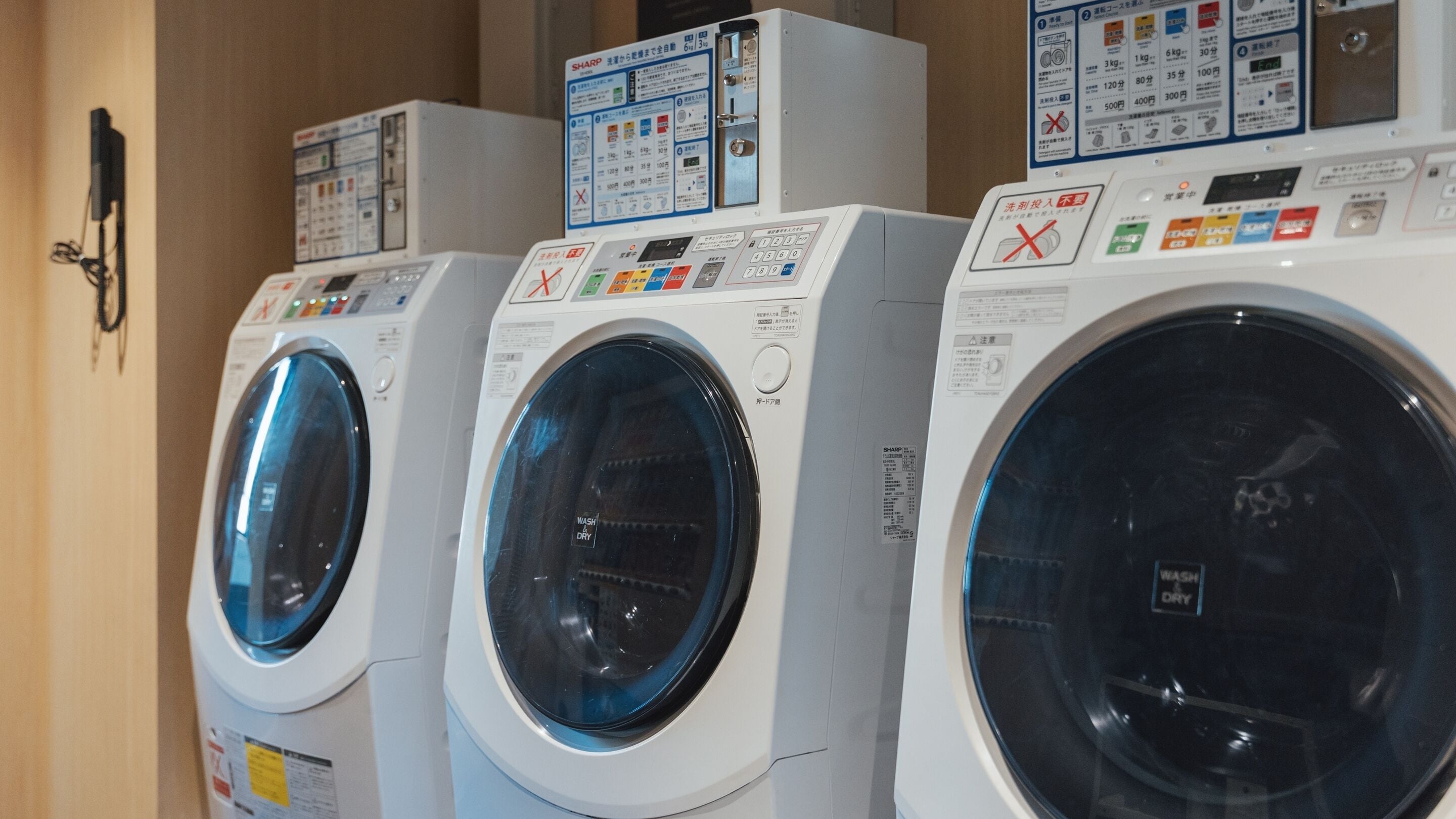 A row of front-loading washing machines with control panels and instruction manuals.